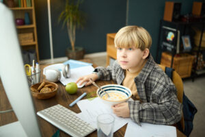 A young boy eats cereal while doing homework