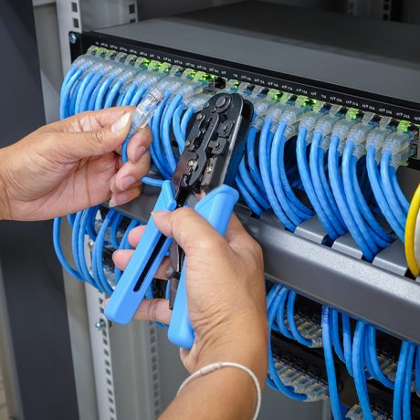 hand of system administrator with network cable connected to patch panel of network gigabit switch and crimping pliers tool