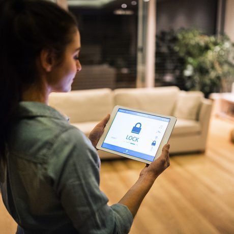 A woman holding a tablet with home security controls